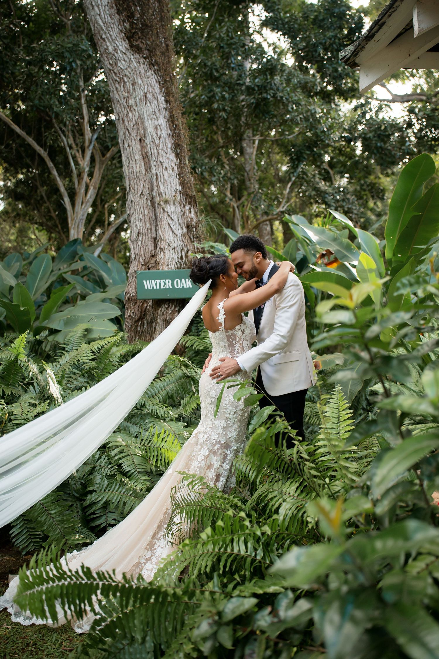 Wedding couple sharing a quiet portrait moment in a lush garden setting with the bride's veil flowing through greenery.